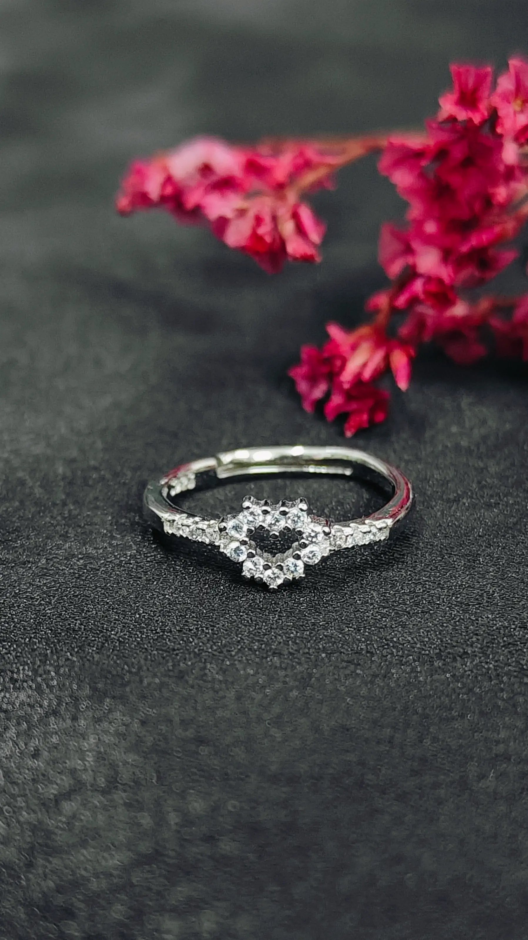 Silver ring with gemstones on a dark surface with pink flowers